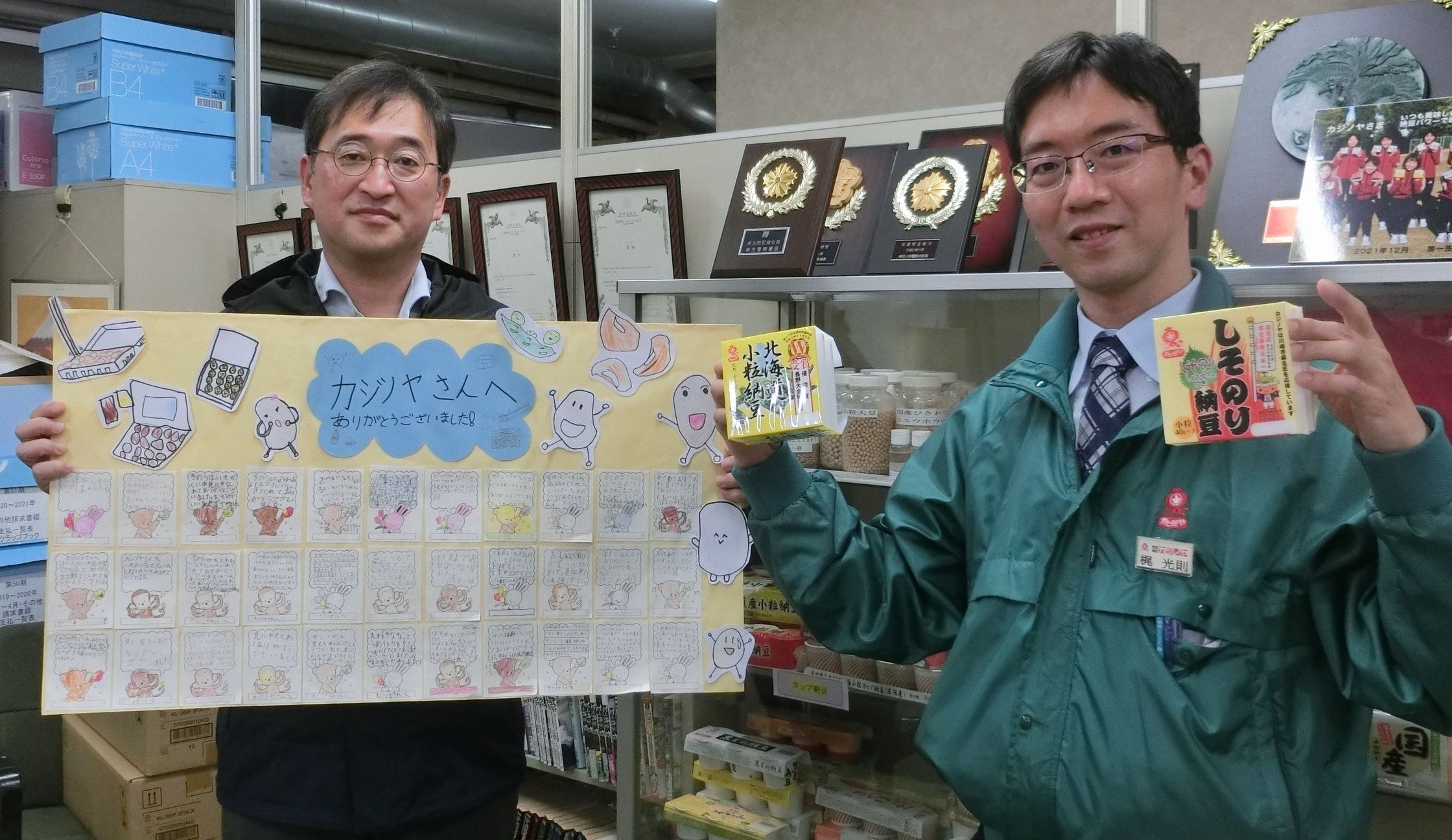 梶光則社長(右)と岡田純常務執行役員(左)、および岡上小学校の生徒から寄せられたカジノヤへの感謝のメッセージ